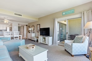 A living room with a television, a sofa, a coffee table, and a dining area with chairs.