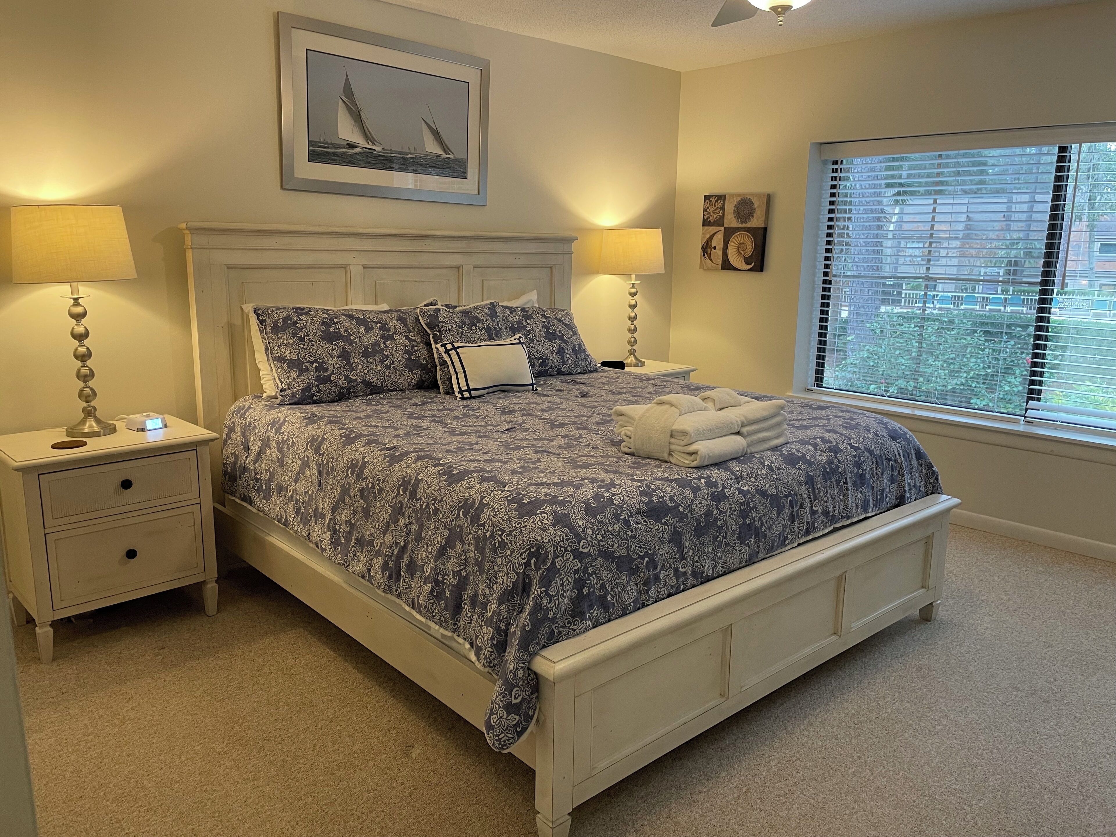 Een keurig opgemaakt slaapkamer met een bed, bedlampen, een lijst met een foto en een raam met jaloezieën.