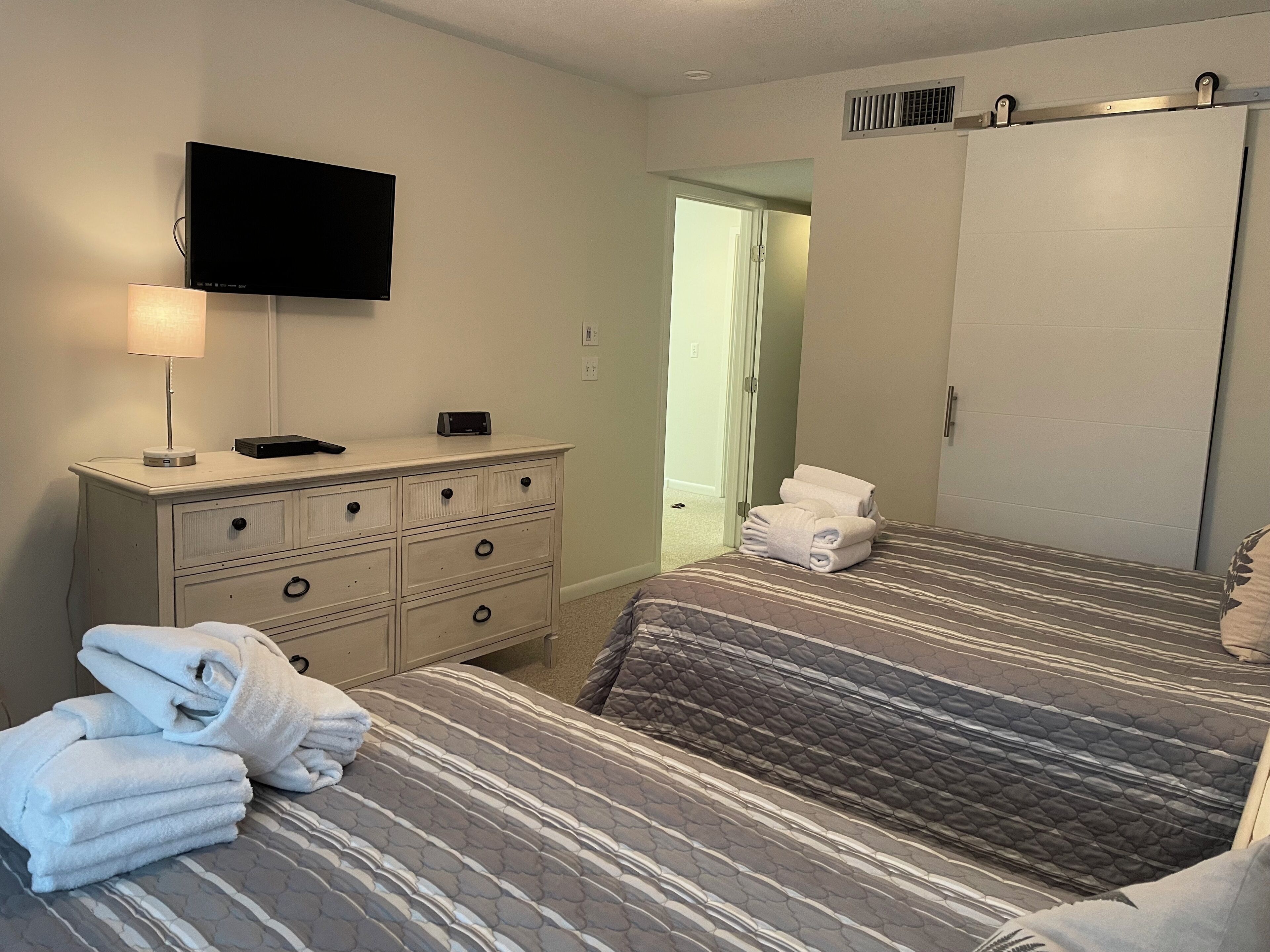Quarto de hotel com duas camas, uma cômoda, uma televisão e um banheiro visível por uma porta aberta.