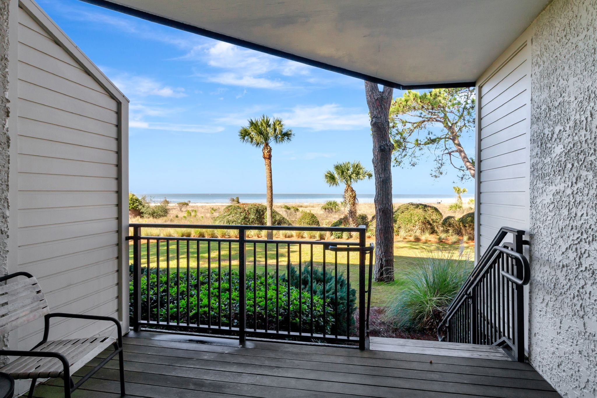 A balcony with a view of the beach, a bench, and a railing.