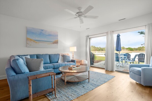 A living room with a blue sofa, a glass coffee table, and a view of the outdoors through a sliding glass door. - 1619 Port Villas at The Sea Pines Resort (Hilton Head Island)