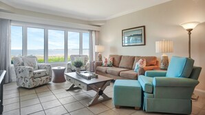 A living room with a view of the sea, a sofa, a chair, a coffee table, and a lamp. - 1829 Beachside Tennis at The Sea Pines Resort (Hilton Head Island)