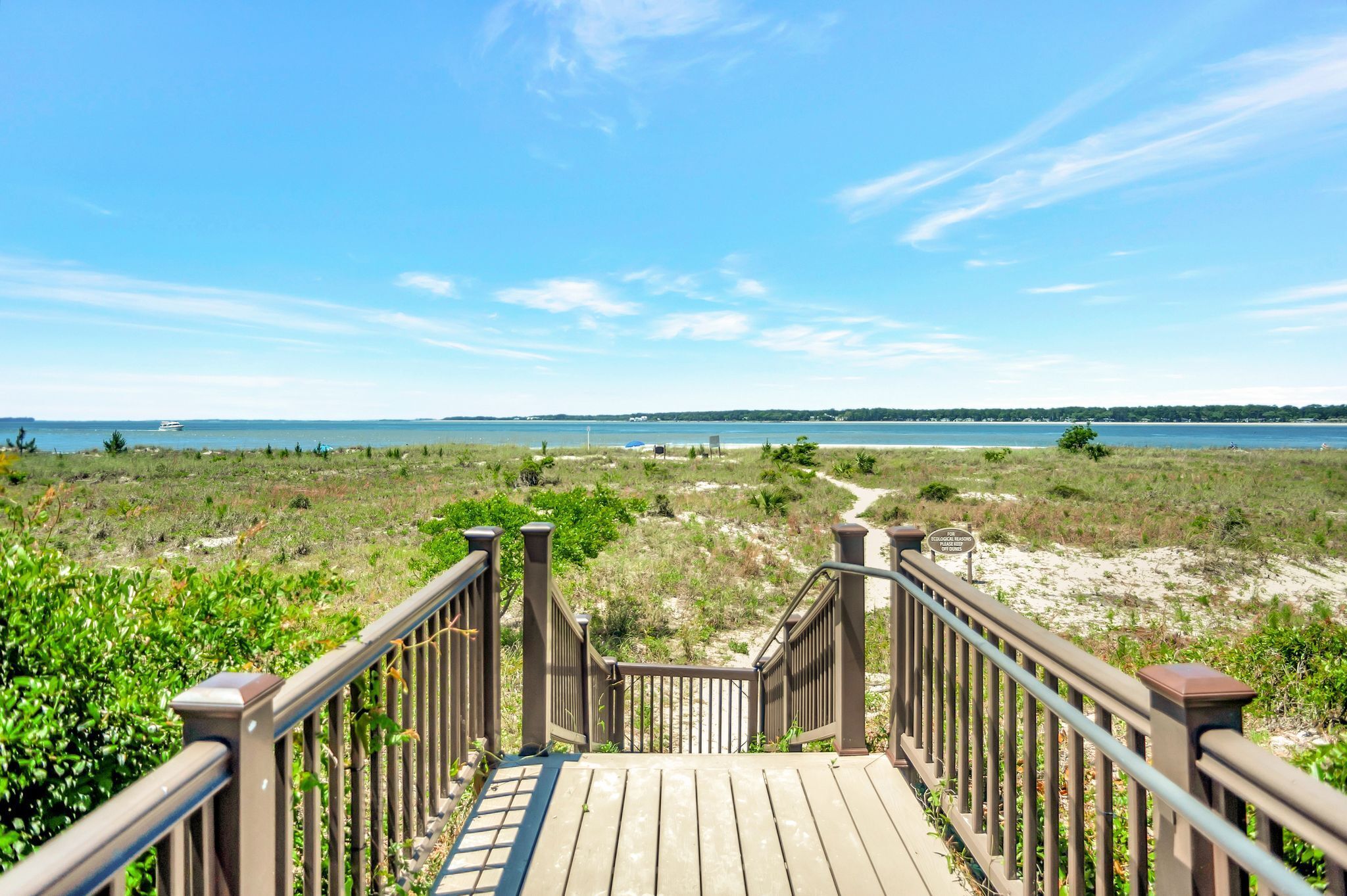 A wooden boardwalk leading to a beach with a clear view of the ocean and distant land.