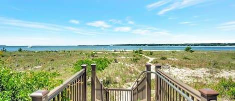 A wooden boardwalk leading to a beach with a clear view of the ocean and distant land.