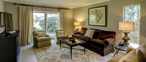 A living room with a sofa, armchairs, a coffee table, a TV, and a lamp.