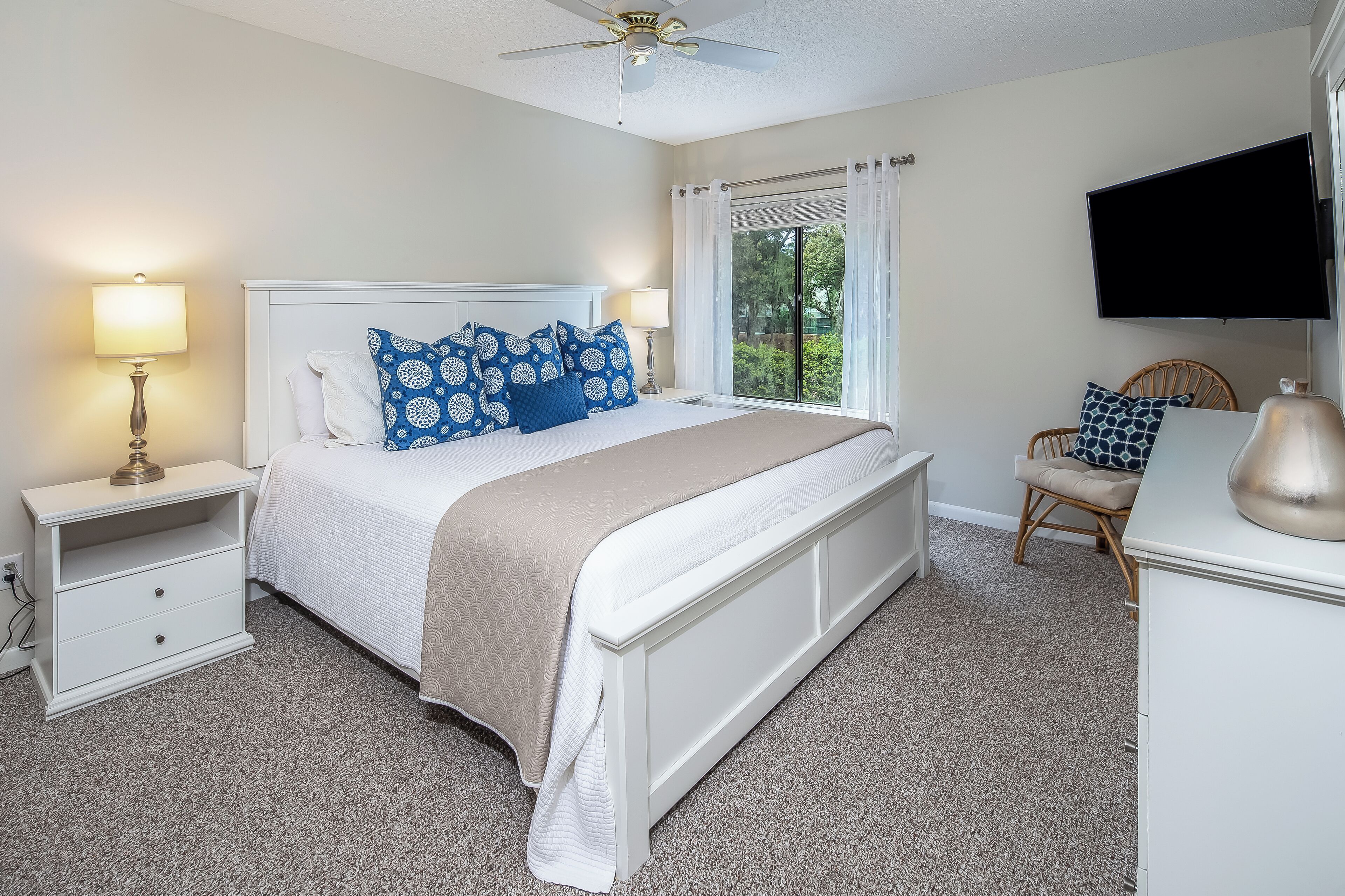 A bedroom with a bed, nightstands, a TV, and a window with curtains.