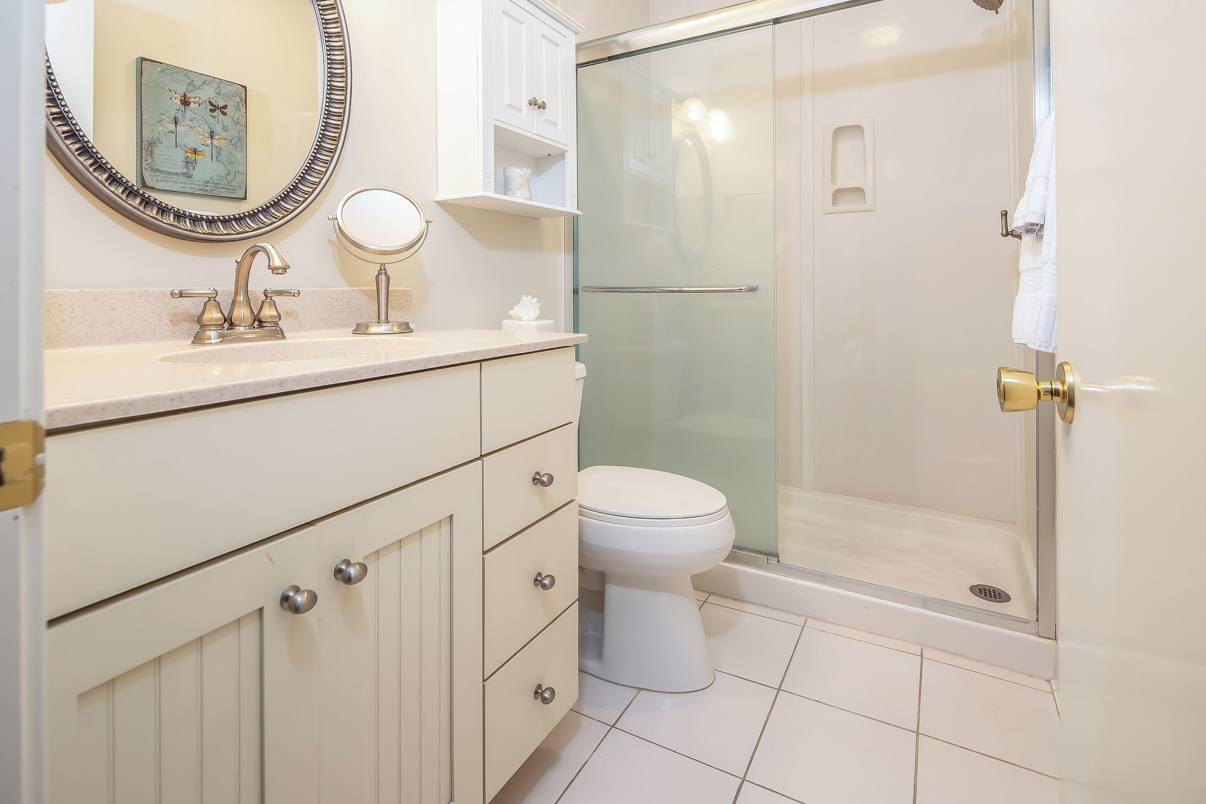 Une salle de bain moderne avec un meuble-lavabo blanc, un miroir rond, des toilettes et une douche à parois de verre.