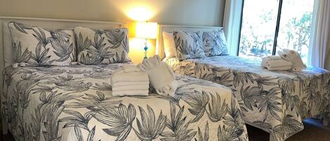 A hotel room with two beds, each with a floral-patterned bedspread, a bedside lamp, and a window with curtains.