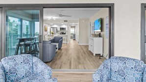 A modern living room with a large sliding glass door leading to a balcony, a kitchen in the background, and a dining area. - Gulf-Front 3BR Sanibel Condo with Stunning Views! (Sanibel)