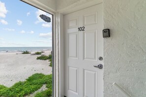 A white door with the number 102, a view of a beach, and a security camera on the wall. - Blue Gulf 102 | Gulf-Front 3BR Sanibel Condo with Stunning Views! (Sanibel)