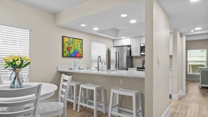 A modern kitchen with white cabinetry, a stainless steel refrigerator, and a dining area with white chairs and a table. - Gulf-Front 3BR Sanibel Condo with Stunning Views! (Sanibel)