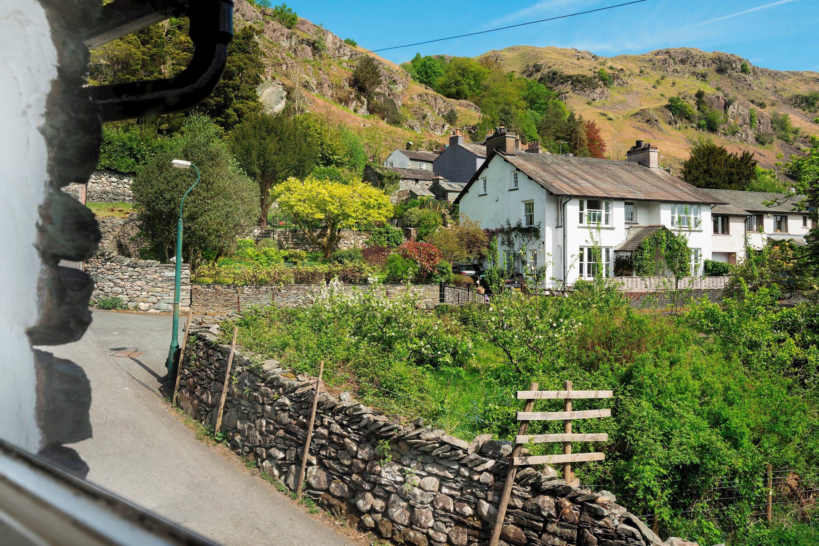 A white building with a stone wall and a wooden fence in a rural setting.