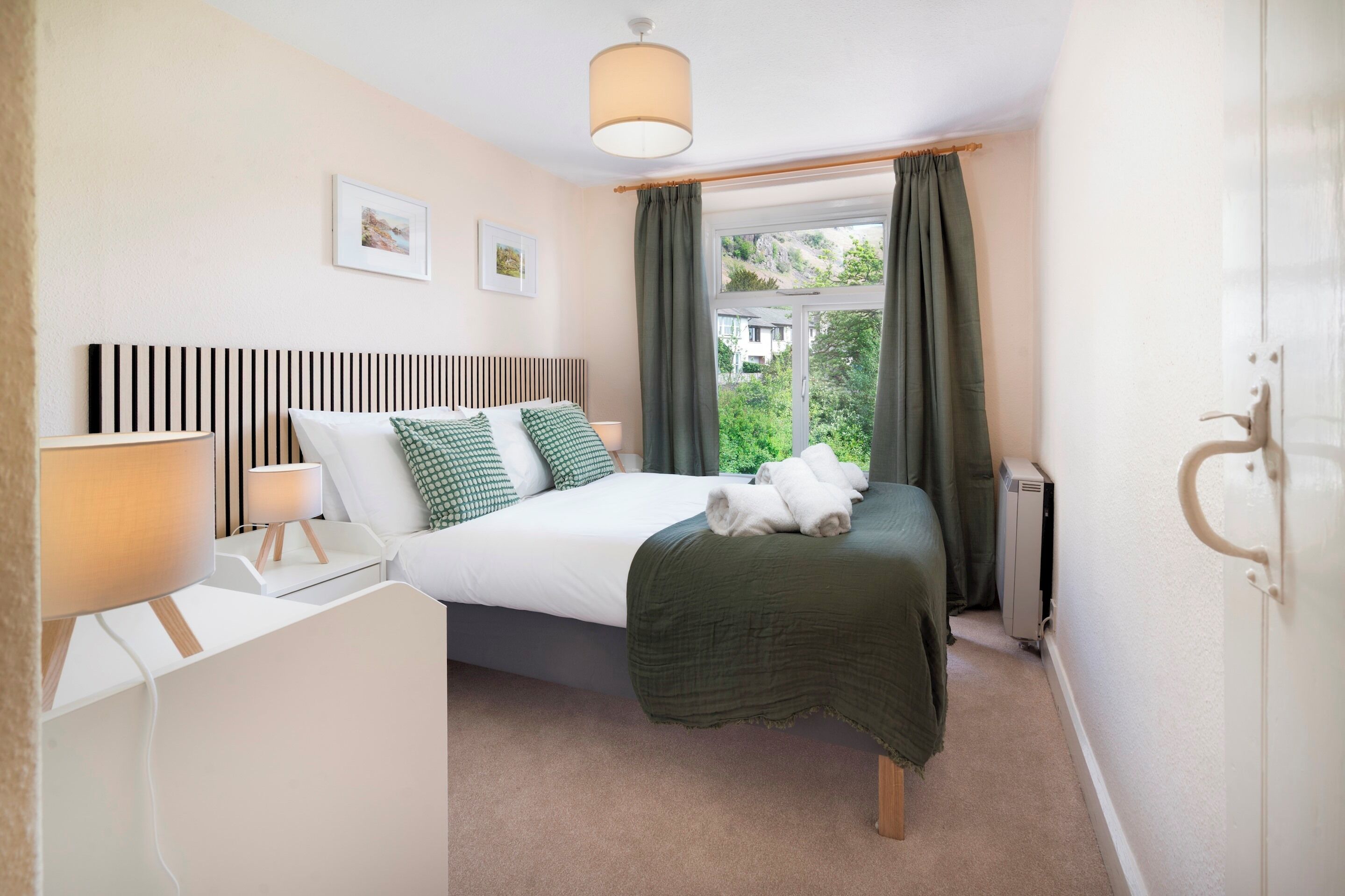 Een slaapkamer met een bed, nachtkastjes, een lamp, een radiator en een raam met gordijnen.