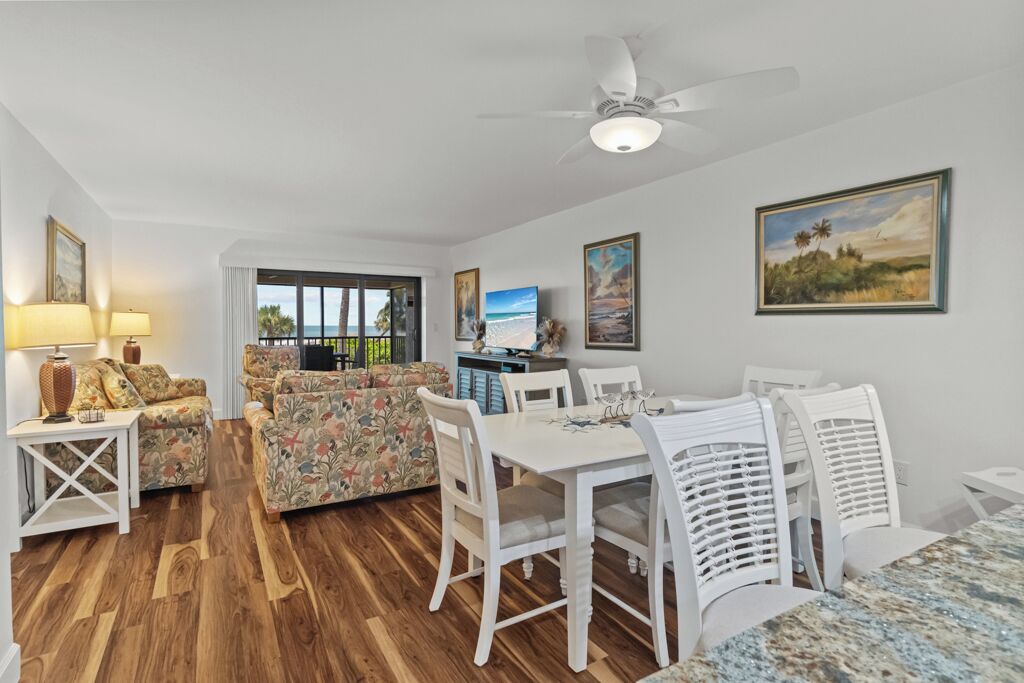 A spacious living area with a wooden floor, a white dining table with chairs, and a sofa set.