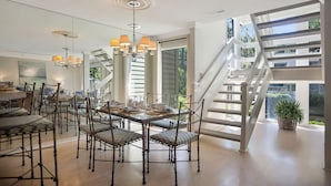 A spacious dining area with a high ceiling, modern chandelier, and a staircase leading to an upper level.