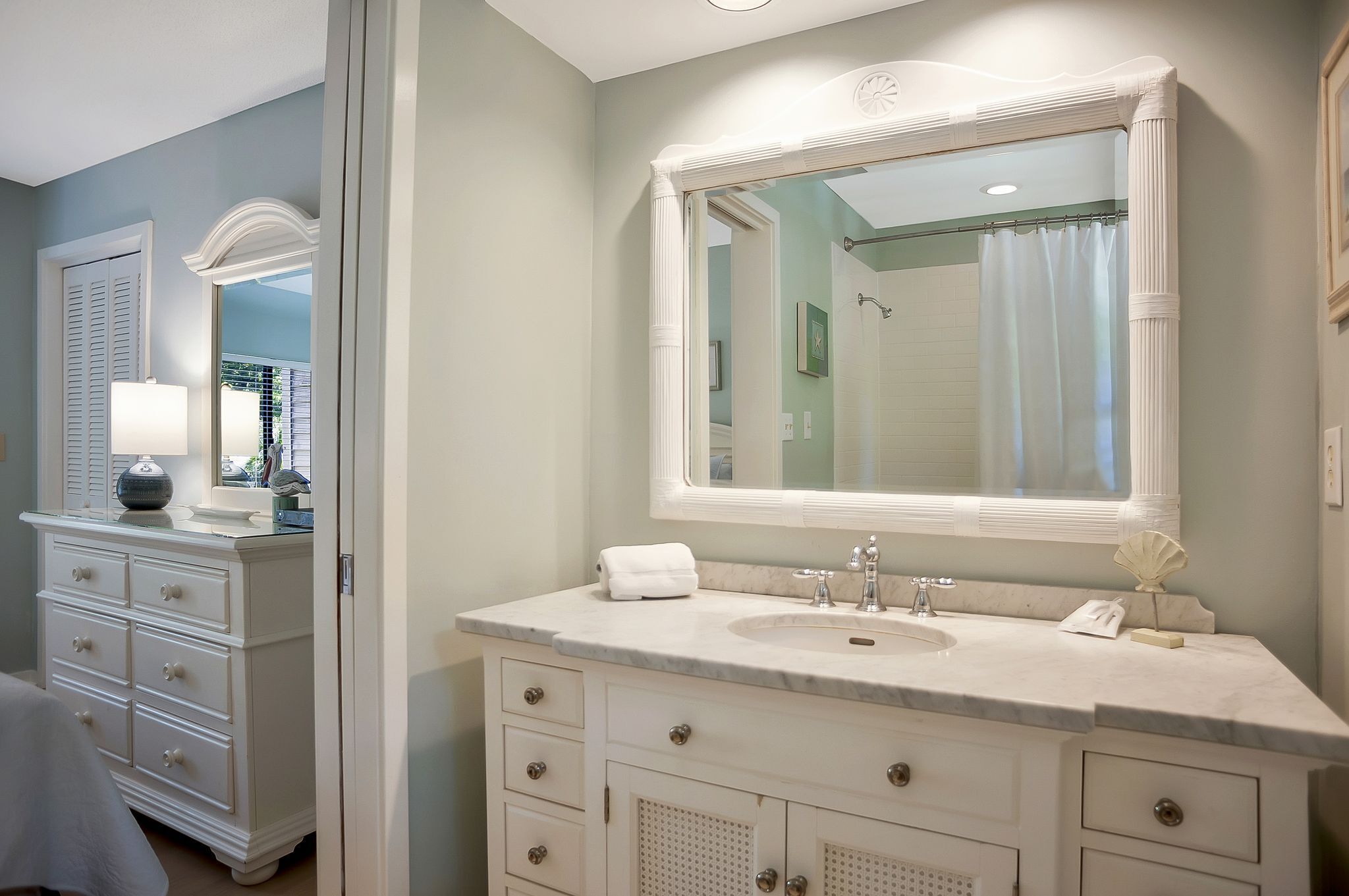 Une salle de bain avec un grand miroir, un meuble-lavabo blanc doté de tiroirs, un évier et une serviette.