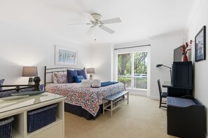 A bedroom with a bed, bedside tables, a desk, a chair, a ceiling fan, and a window with blinds. - 2410 Lighthouse Tennis at The Sea Pines Resort (Hilton Head Island)