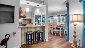 Una cucina moderna con isola centrale, sgabelli da bar in legno e zona pranzo con tavolo e sedie.