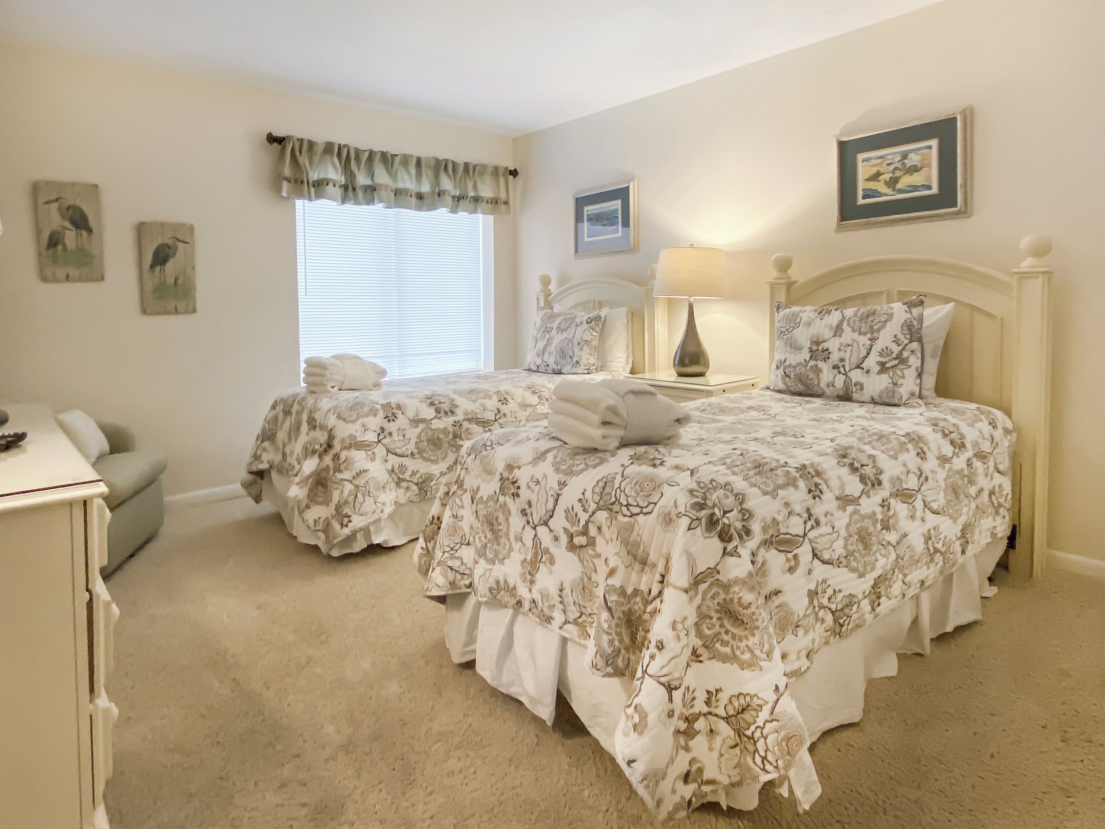 A bedroom with two beds, a nightstand, a lamp, and a window with blinds.