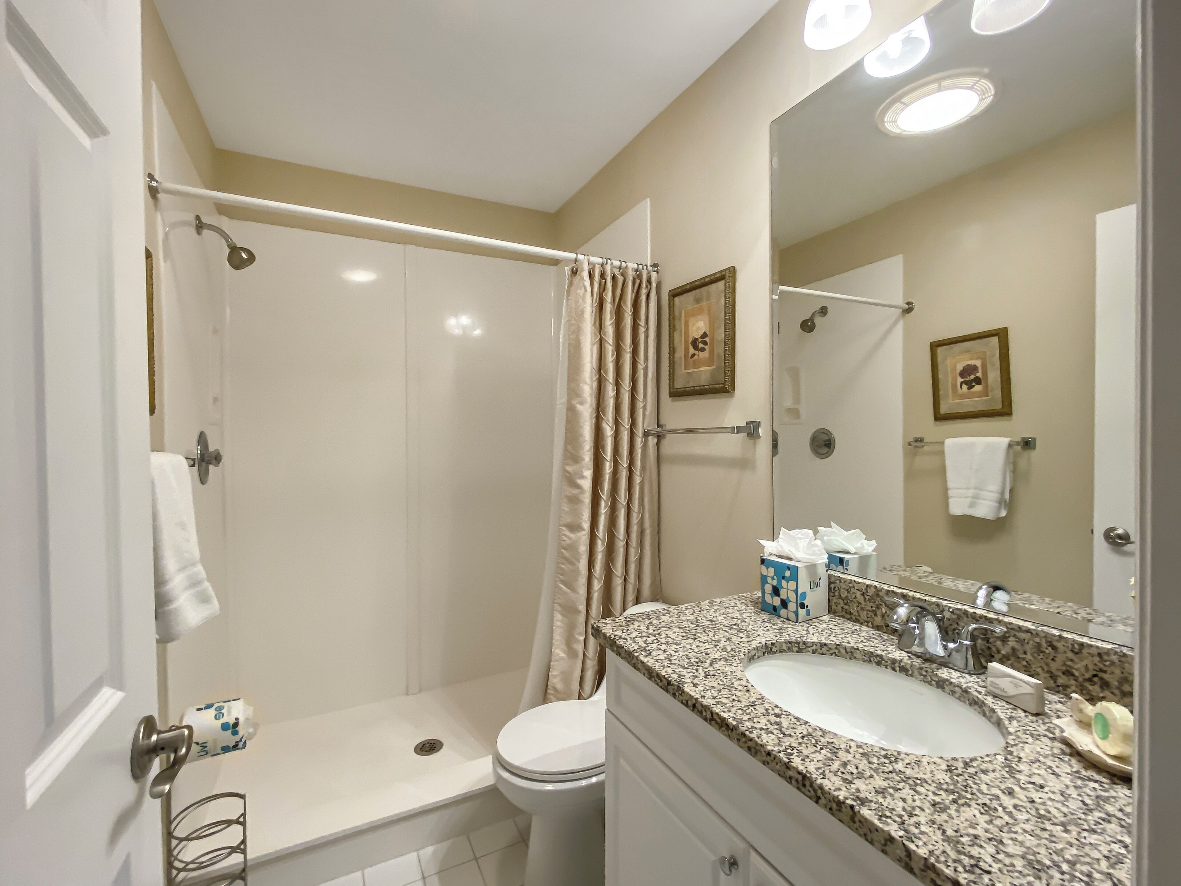 A bathroom with a shower, toilet, sink, and a large mirror.