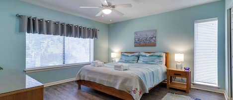 Une chambre à coucher avec un lit en bois, un ventilateur de plafond, une table de chevet avec une lampe et une fenêtre avec des stores.
