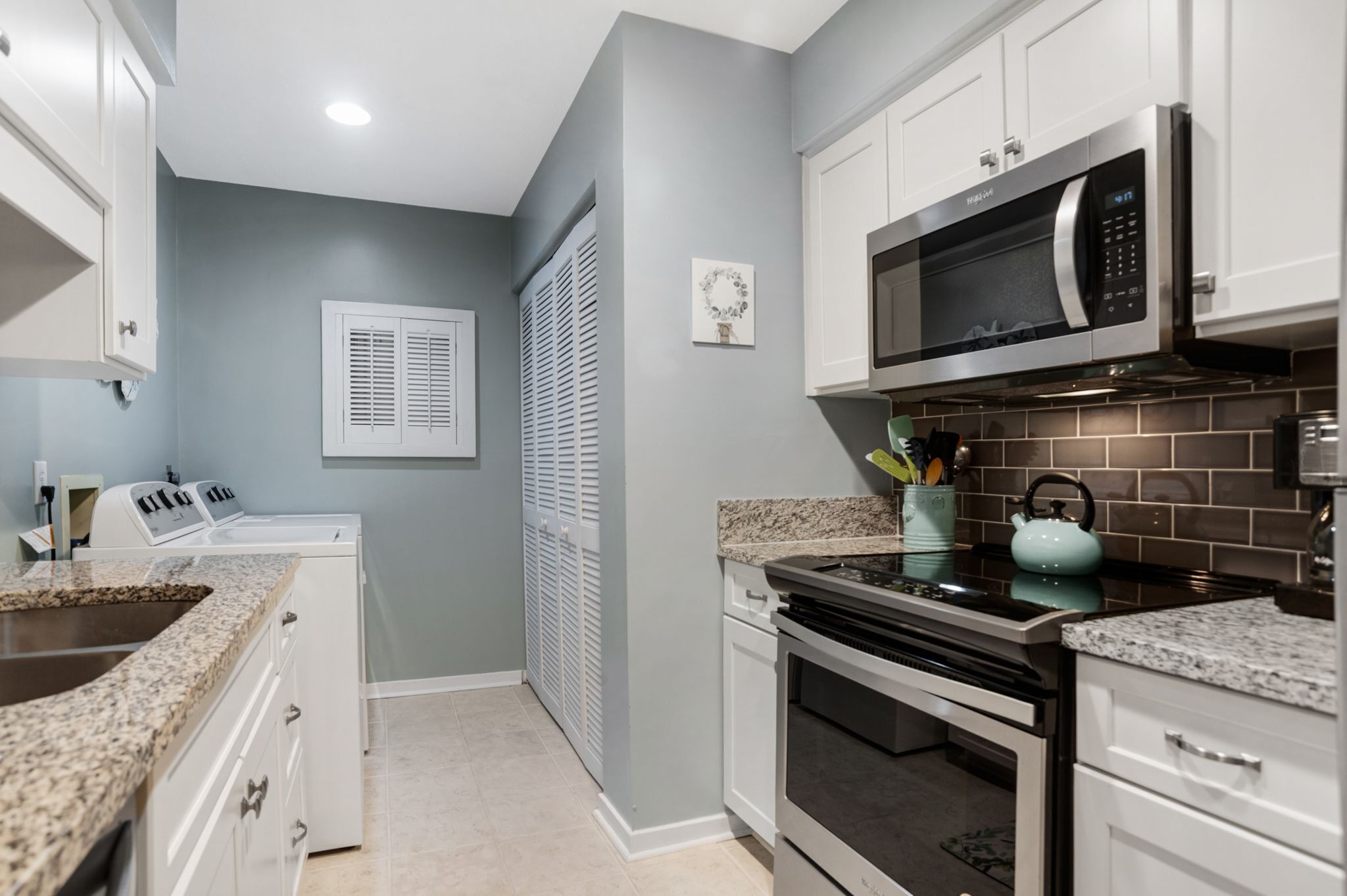A kitchen with white cabinets, a stainless steel microwave, a stove, and a sink.