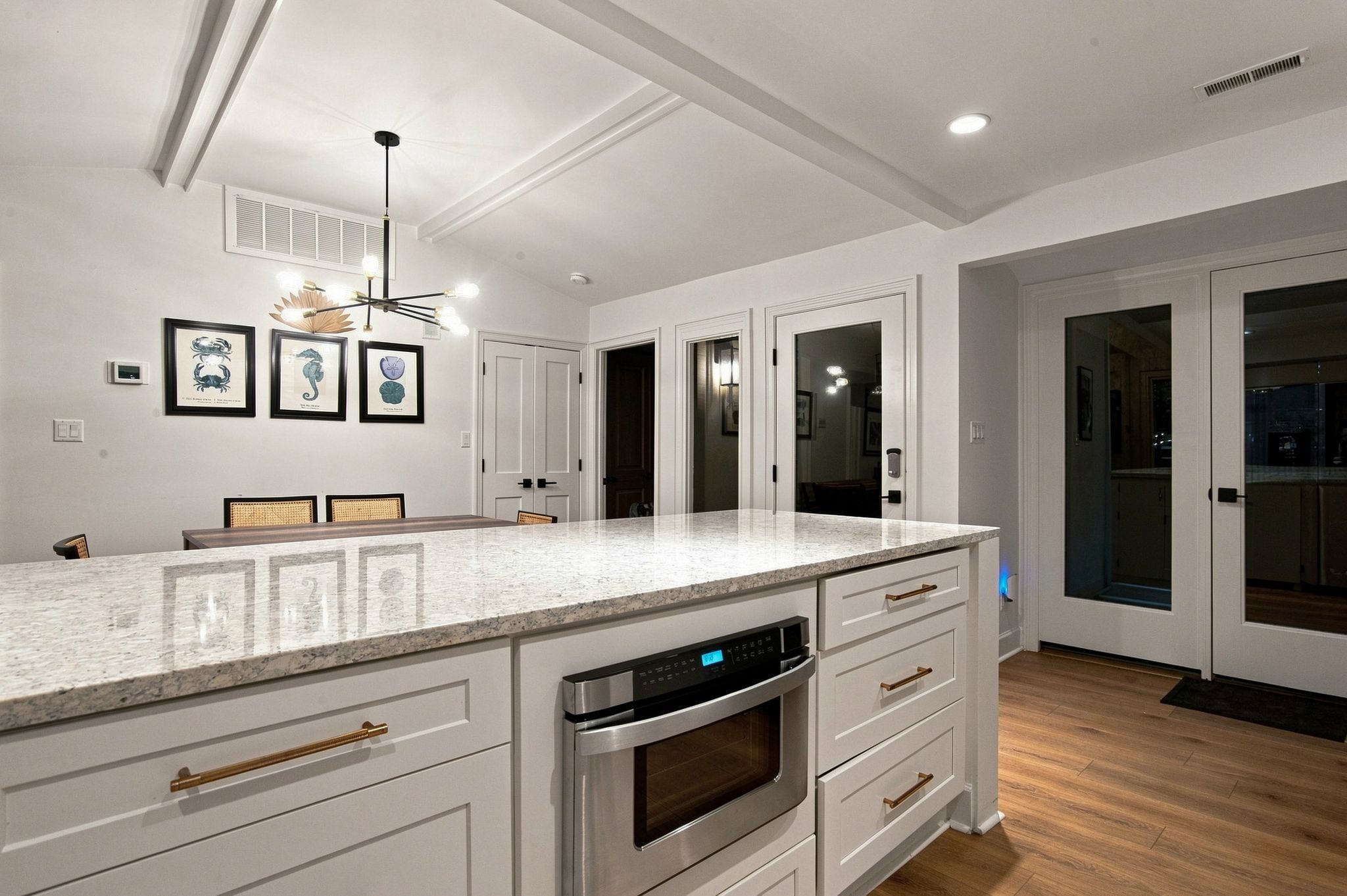 A modern kitchen with white cabinetry, a built-in oven, and a large island with a marble countertop.