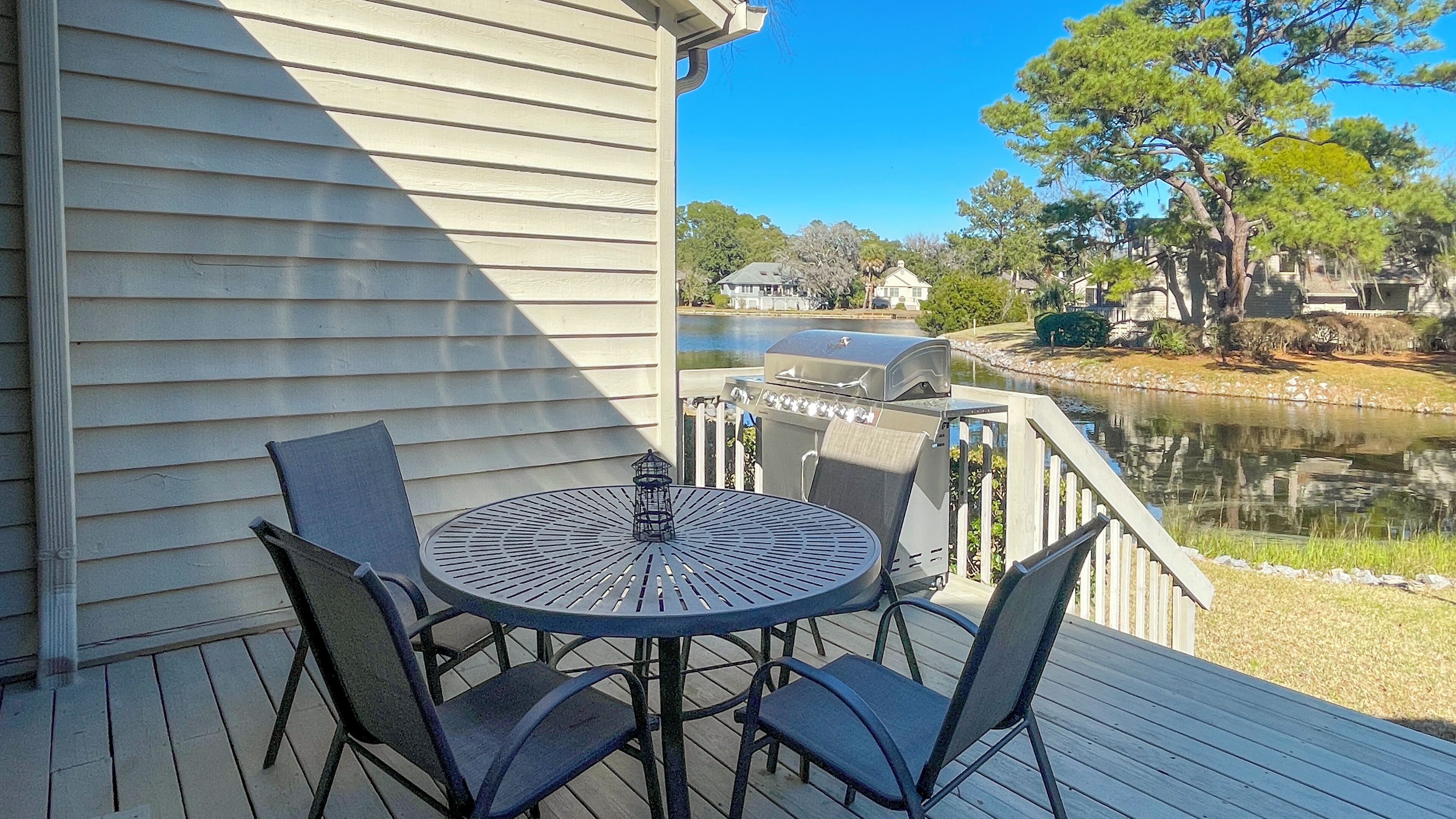 A deck with a round table and four chairs, overlooking a body of water and a row of houses.