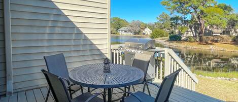 A deck with a round table and four chairs, overlooking a body of water and a row of houses.