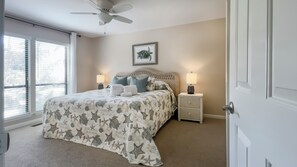 A bedroom with a bed, two bedside tables, a ceiling fan, a window with blinds, and a framed picture on the wall. - 2622 Calibogue Club at The Sea Pines Resort (Hilton Head Island)
