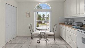 Een keuken met witte kasten, een ronde tafel met stoelen en uitzicht door een raam.