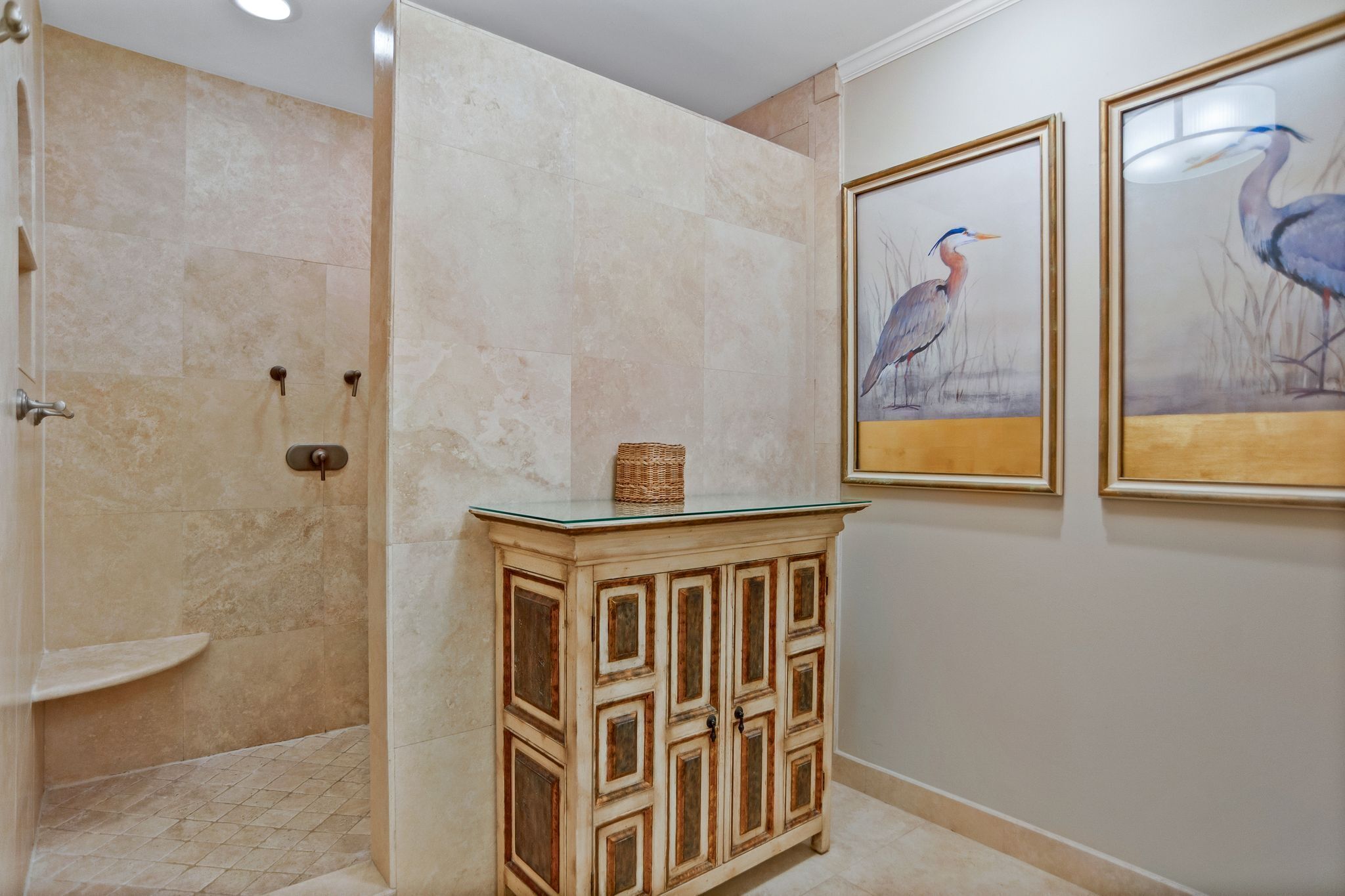 A bathroom with a shower, a glass-top vanity, and two framed bird paintings on the wall.