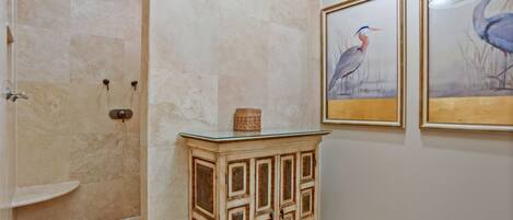 A bathroom with a shower, a glass-top vanity, and two framed bird paintings on the wall.