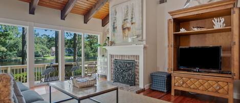 A spacious living room with a fireplace, large windows, and a television on a wooden stand.