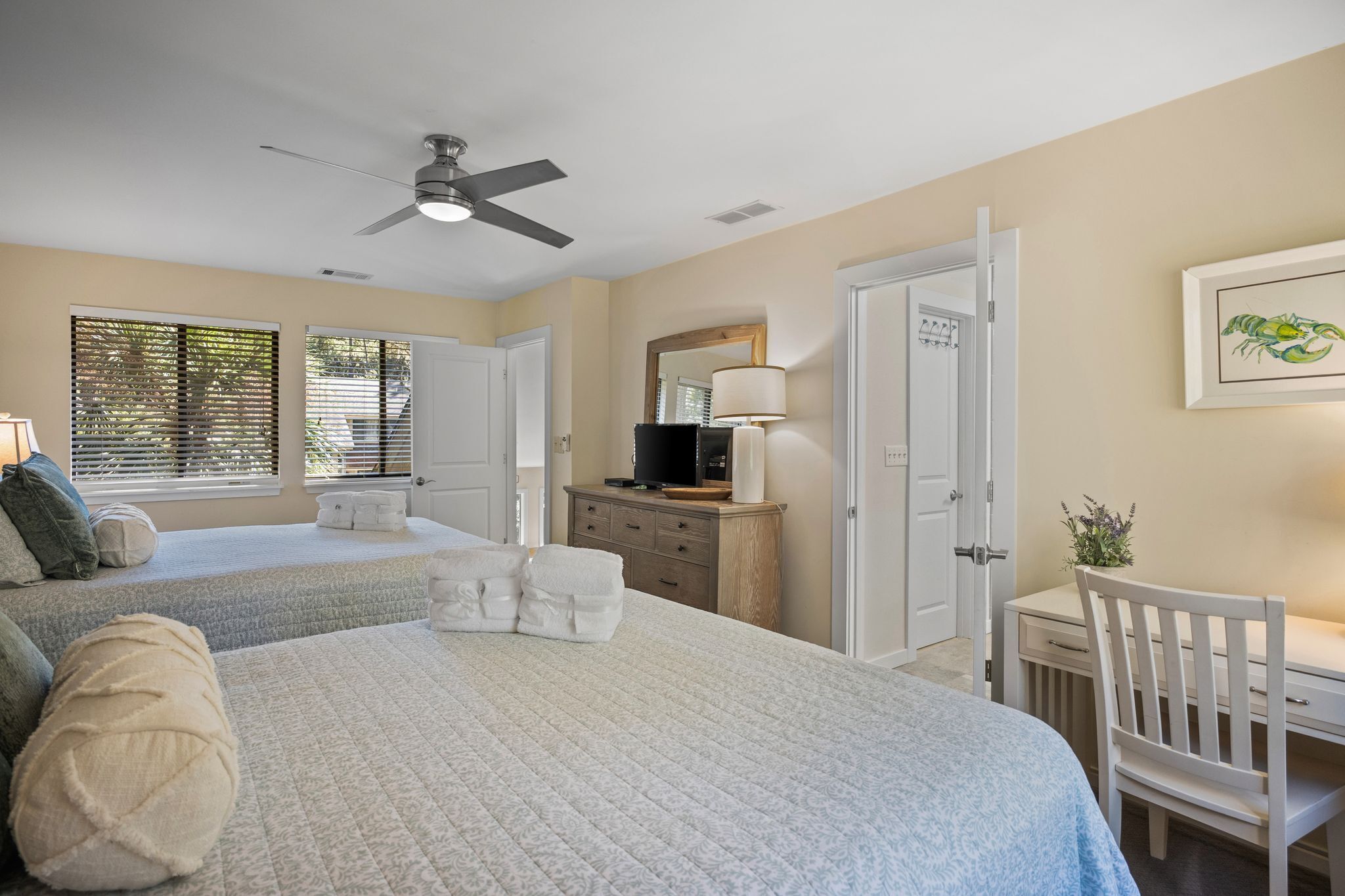 A bedroom with two beds, a desk, a chair, a ceiling fan, and a window with blinds.