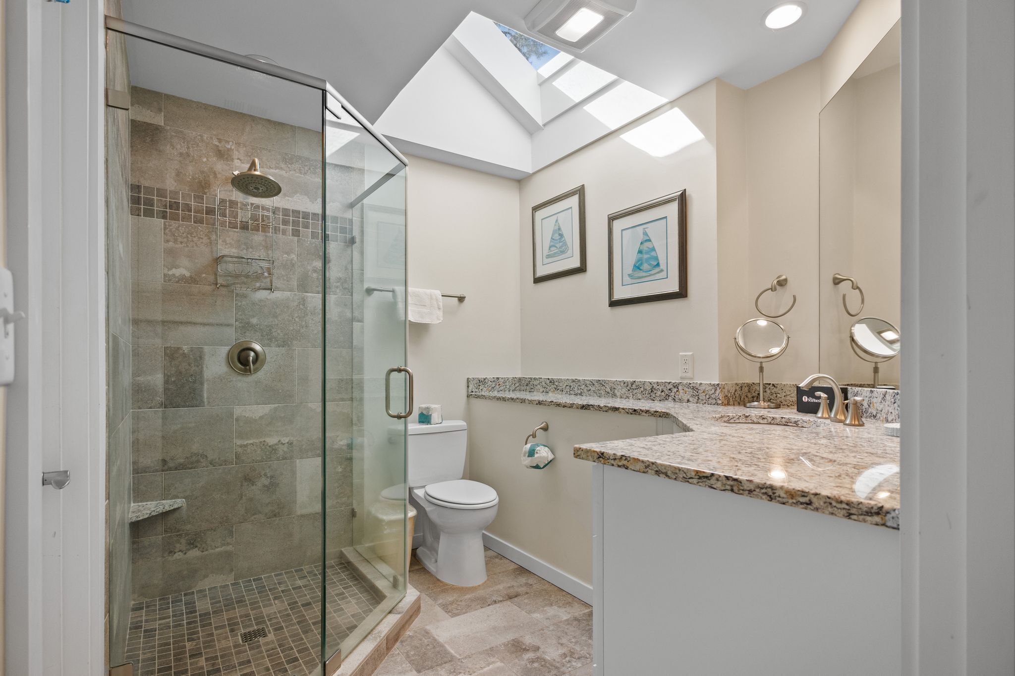 Un baño moderno con ducha de vidrio, inodoro y tocador con encimera de granito.