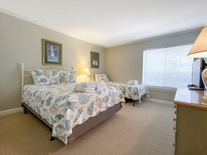 Habitación con dos camas, cada una con ropa de cama floral a juego, una lámpara de noche y una ventana con persianas.