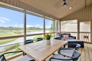 An outdoor deck with a wooden table and chairs, a cushioned seating area, and a view of a lake and golf course. - 6966 Fairway One at The Sea Pines Resort (Hilton Head Island)