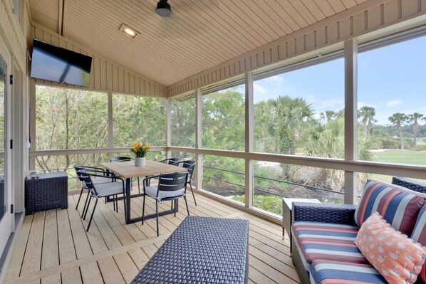 Un espace extérieur abrité doté d’une terrasse en bois, d’une table avec des chaises, d’un canapé et d’un téléviseur fixé au plafond.