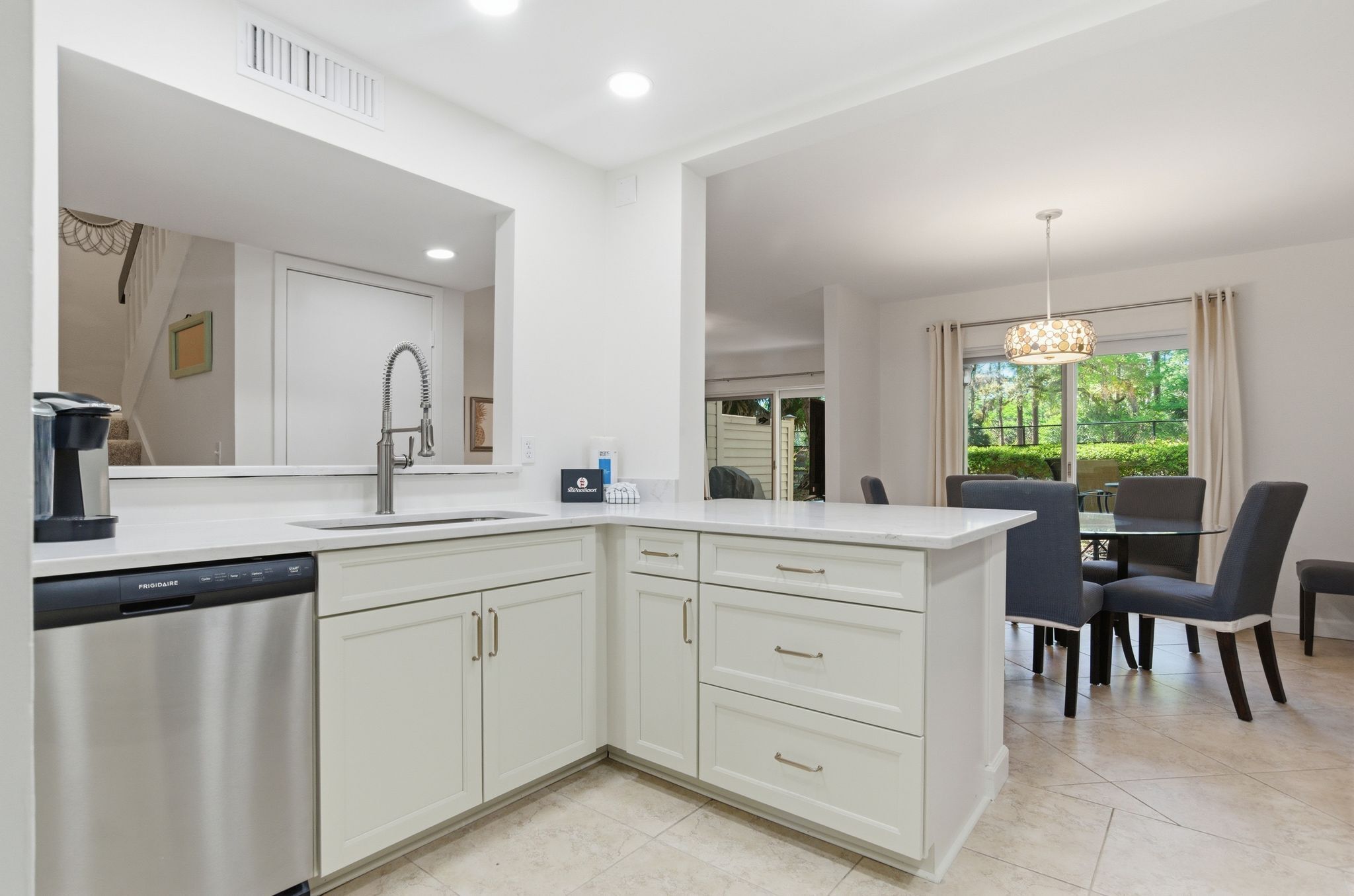 A modern kitchen with white cabinetry, a dishwasher, and a dining area with a table and chairs.