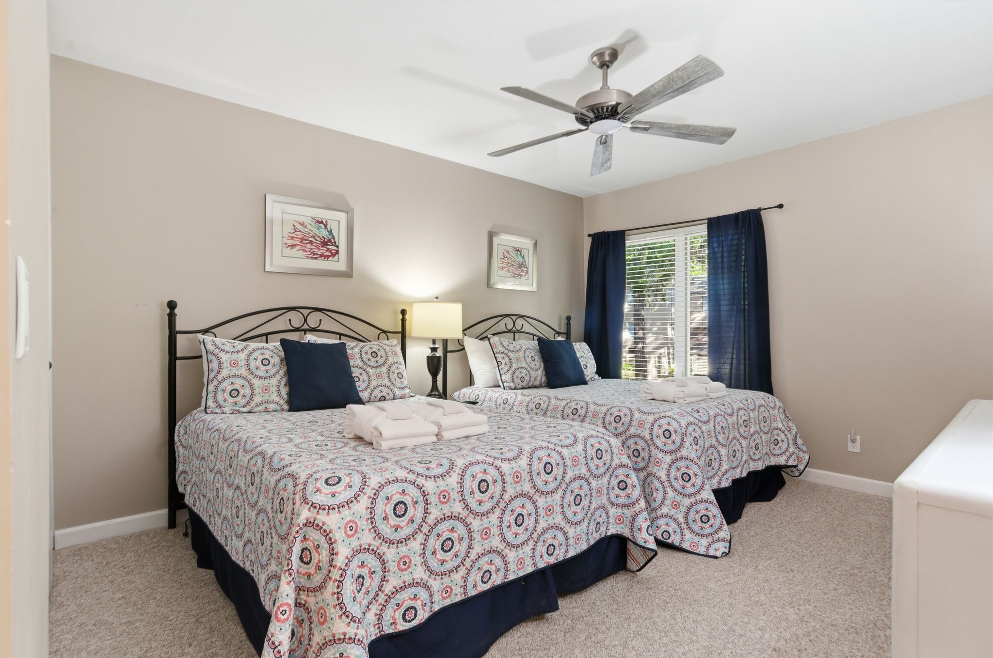 A bedroom with two beds, a ceiling fan, and a window with curtains.
