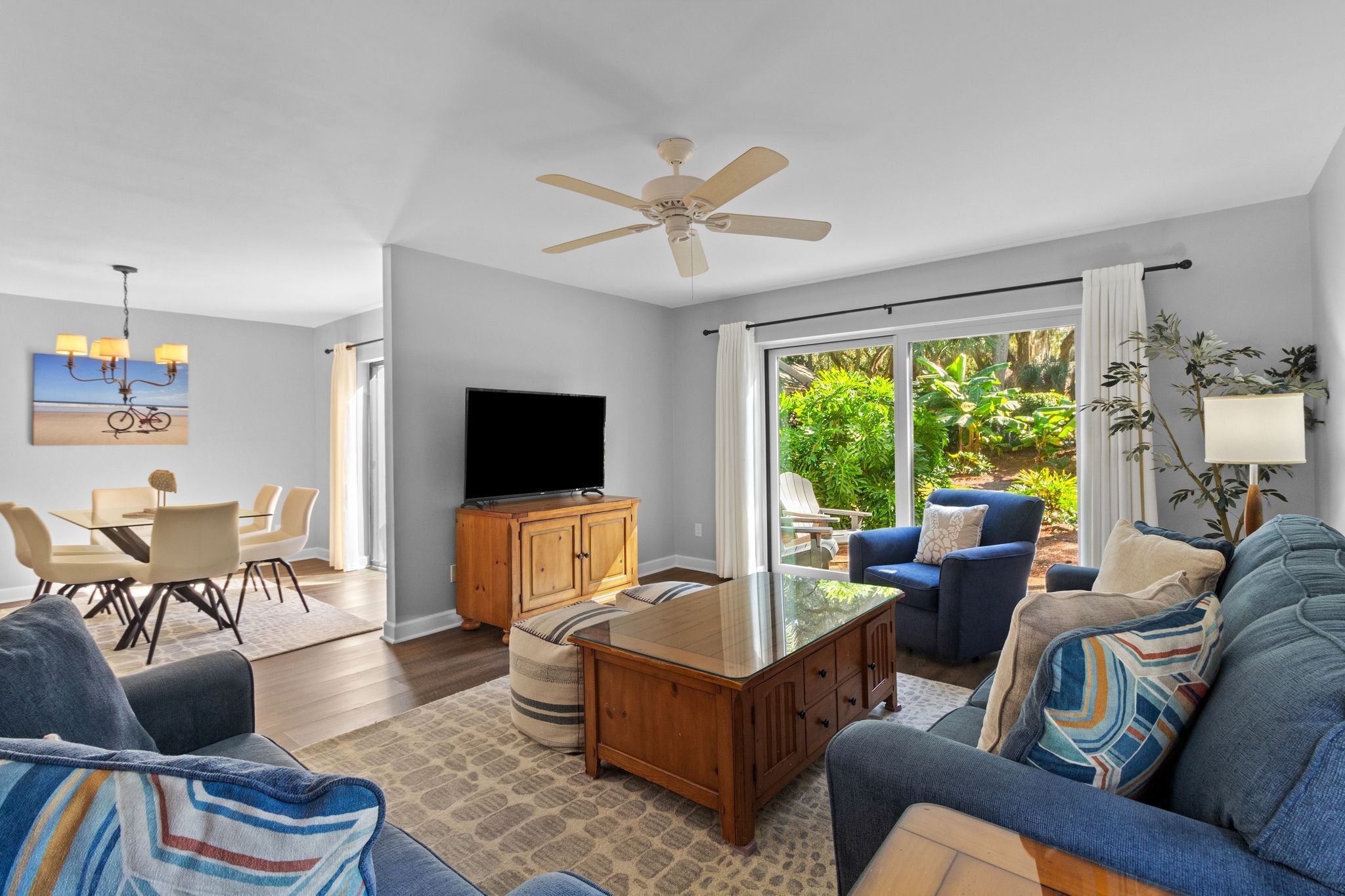 A modern living room with a flat-screen TV, a ceiling fan, and a dining area with a table and chairs.