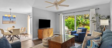 A modern living room with a flat-screen TV, a ceiling fan, and a dining area with a table and chairs.