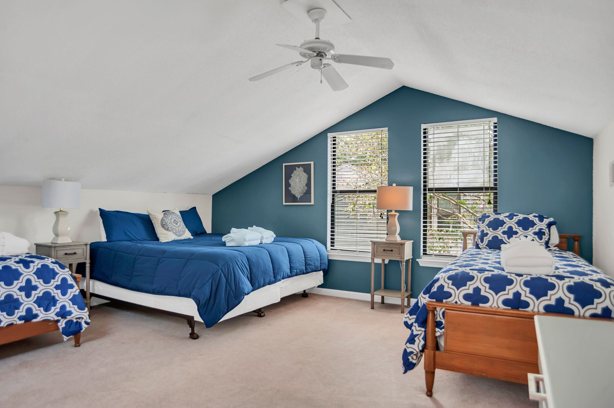 A bedroom with two beds, a ceiling fan, and a window with blinds.