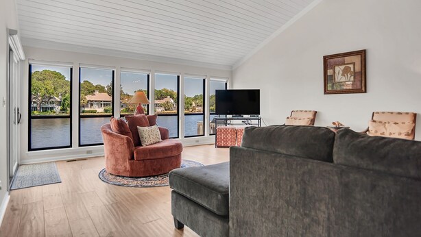 A spacious living room with a large window overlooking a body of water, a flat-screen TV, and a ceiling fan. - 2629 Calibogue Club at The Sea Pines Resort (Hilton Head Island)