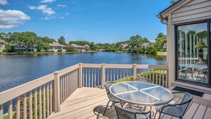 A deck with a table and chairs overlooking a lake, surrounded by houses and greenery. - 2629 Calibogue Club at The Sea Pines Resort (Hilton Head Island)
