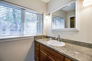 Ein Badezimmer mit Waschbecken, Holzschränken, einer Granitarbeitsplatte und einem Fenster mit Jalousien.