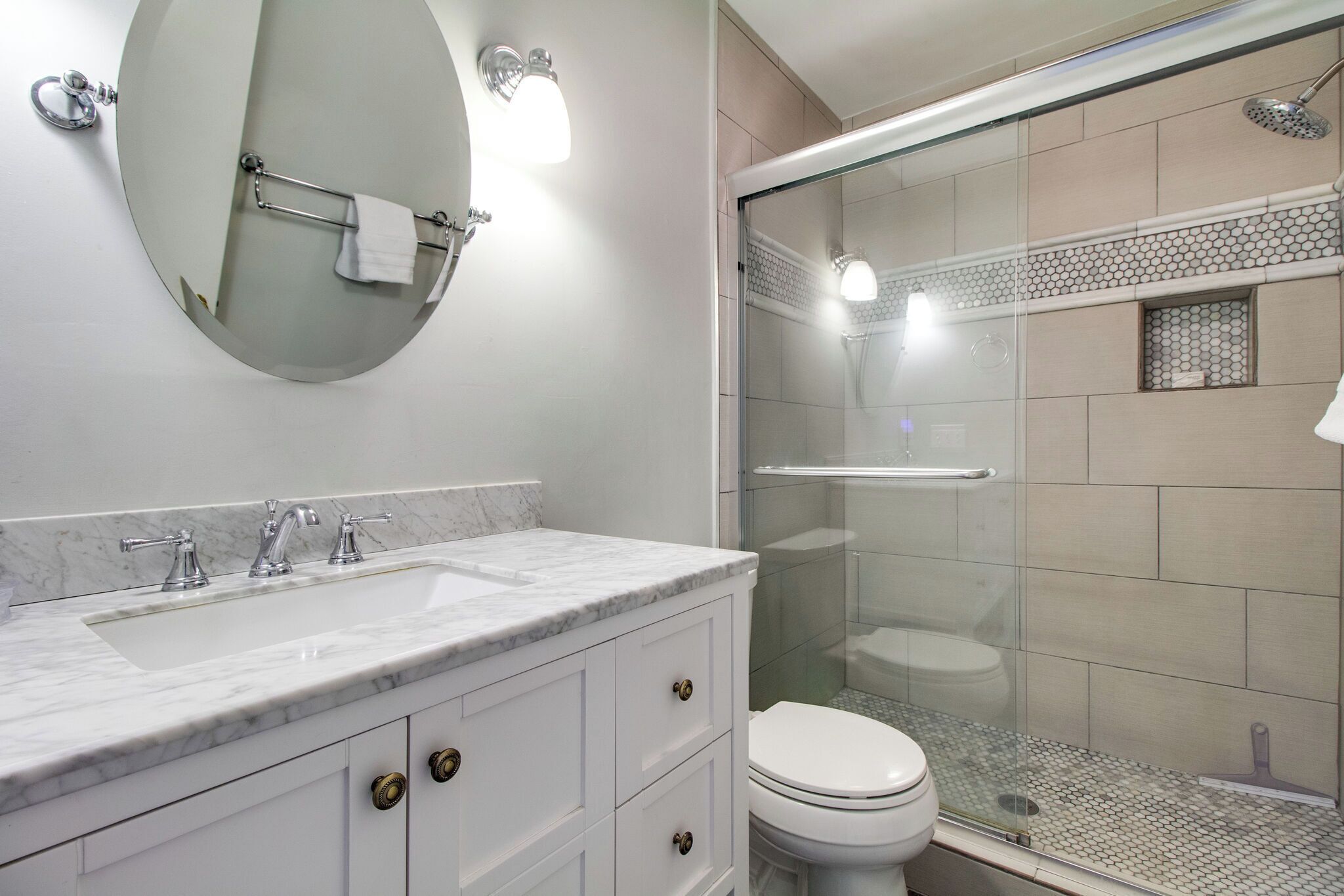 Een badkamer met een marmeren wastafel, een toilet en een douche met glazen wanden.
