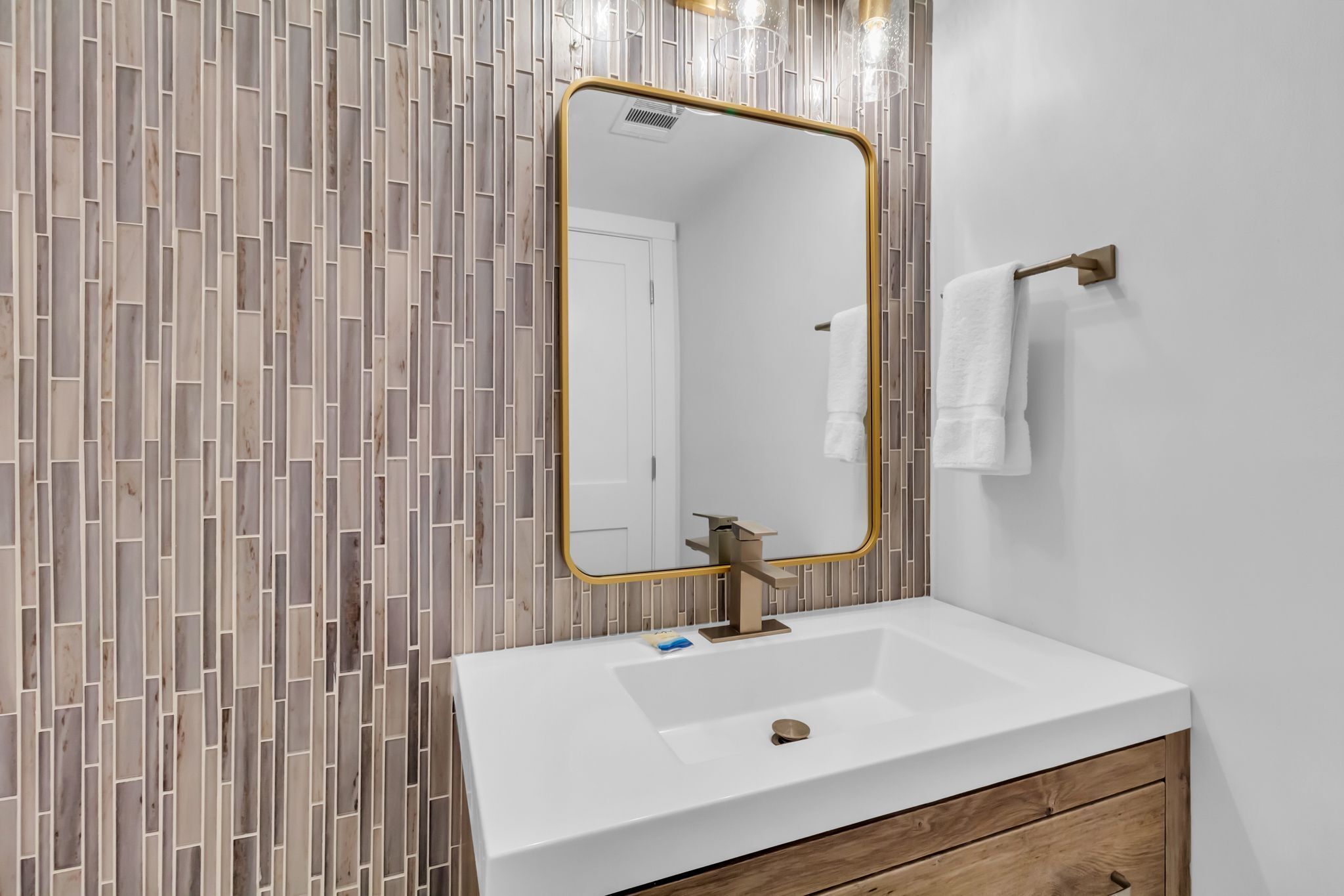 A bathroom with a white sink, a gold-framed mirror, and a tiled wall.