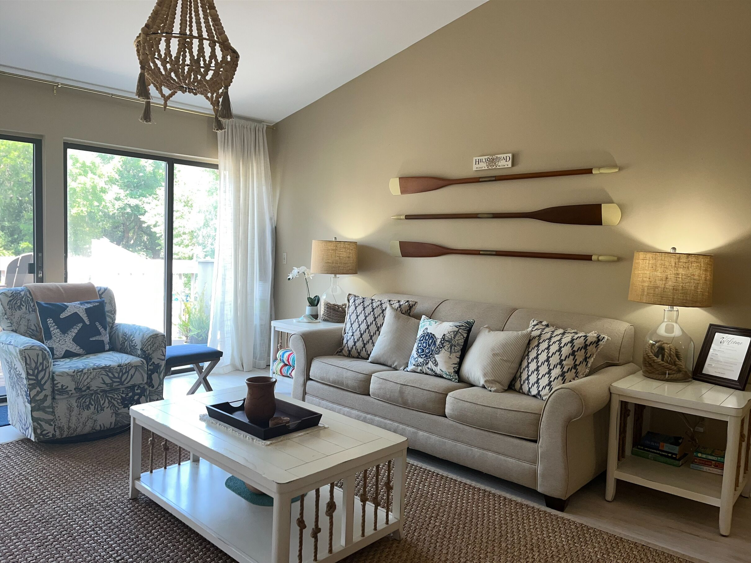 Een woonkamer met een bank, fauteuil, salontafel en twee lampen. Boven de bank hangen twee houten riemen.